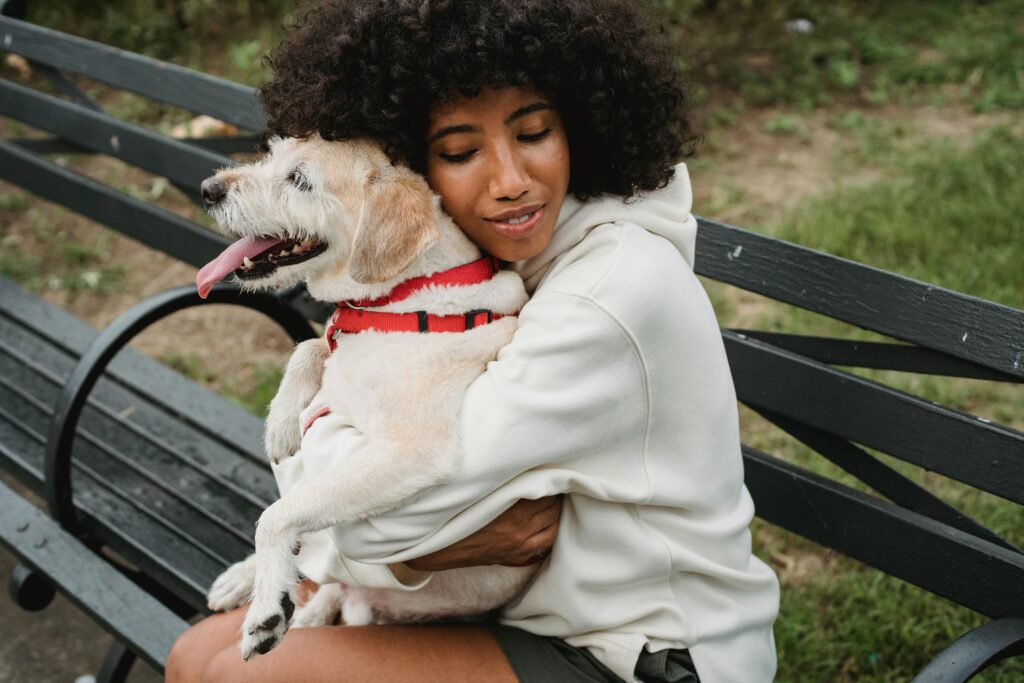 A woman with curly hair embracing her dog on a park bench, capturing pure affection and joy.