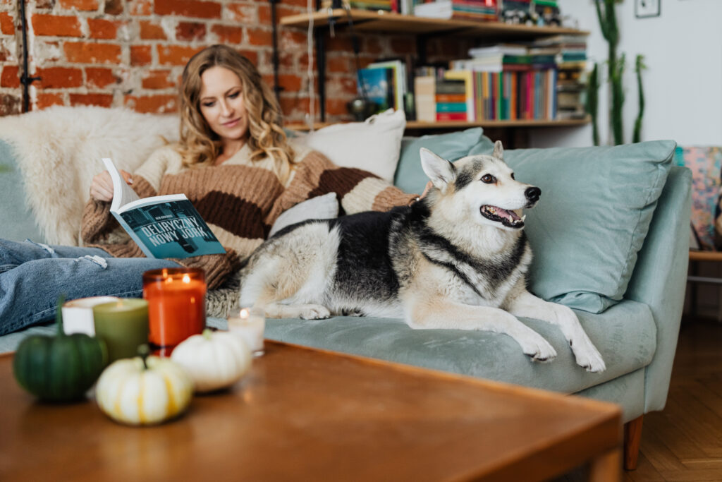 A woman relaxes on a sofa with her Siberian Husky, enjoying a peaceful afternoon with a book.