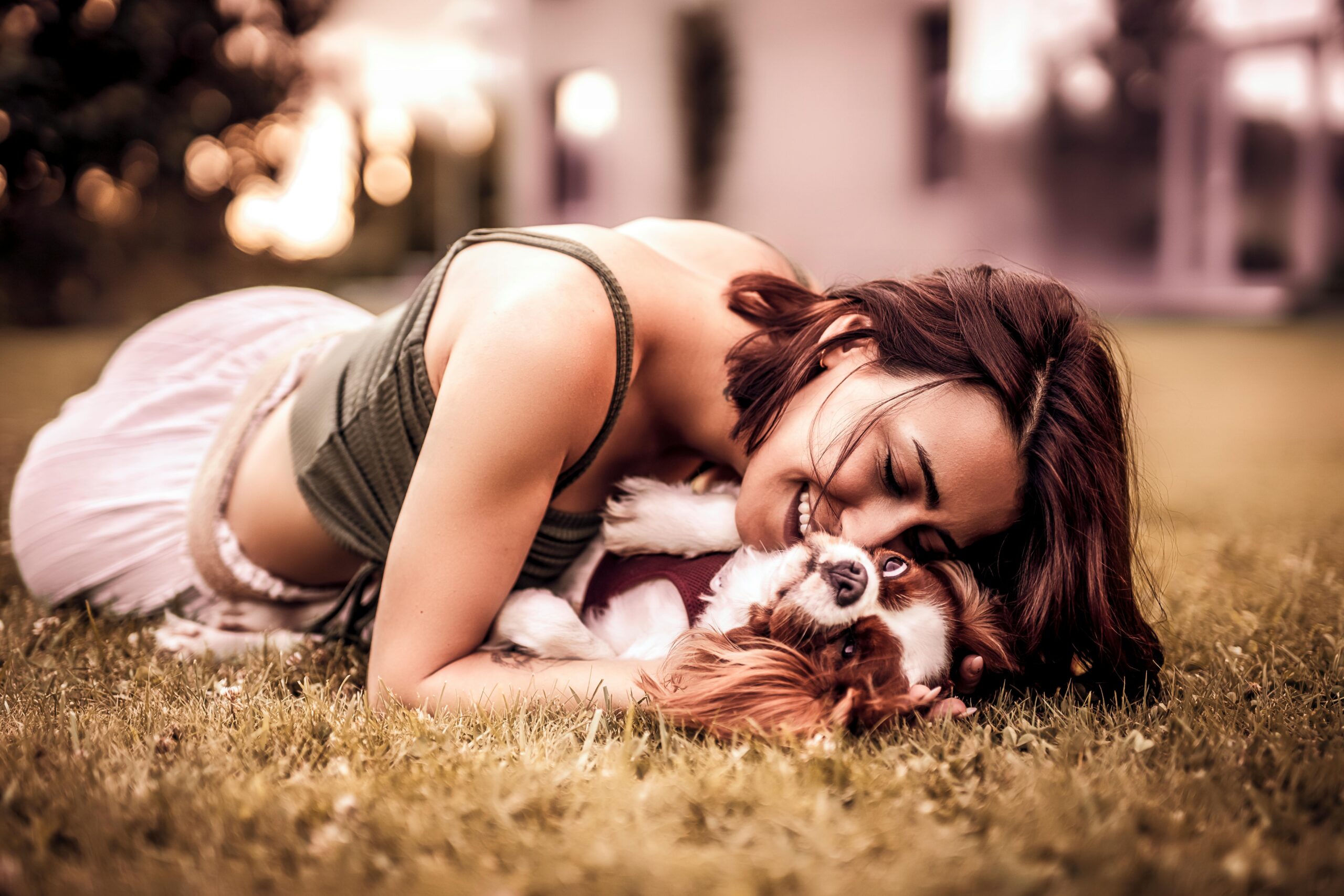 A woman happily cuddling with her Cavalier King Charles Spaniel on the grass.