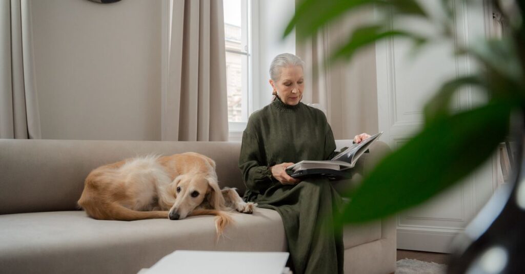Senior woman reads a book on a sofa with her greyhound, enjoying a peaceful afternoon at home.