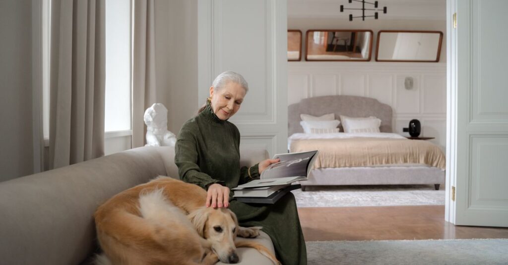Senior woman reading on a sofa while petting her greyhound dog in a cozy living room.