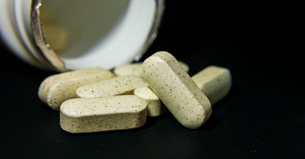 Close-up of white capsule pills spilled from a bottle on a black background. Ideal for health-related visuals.