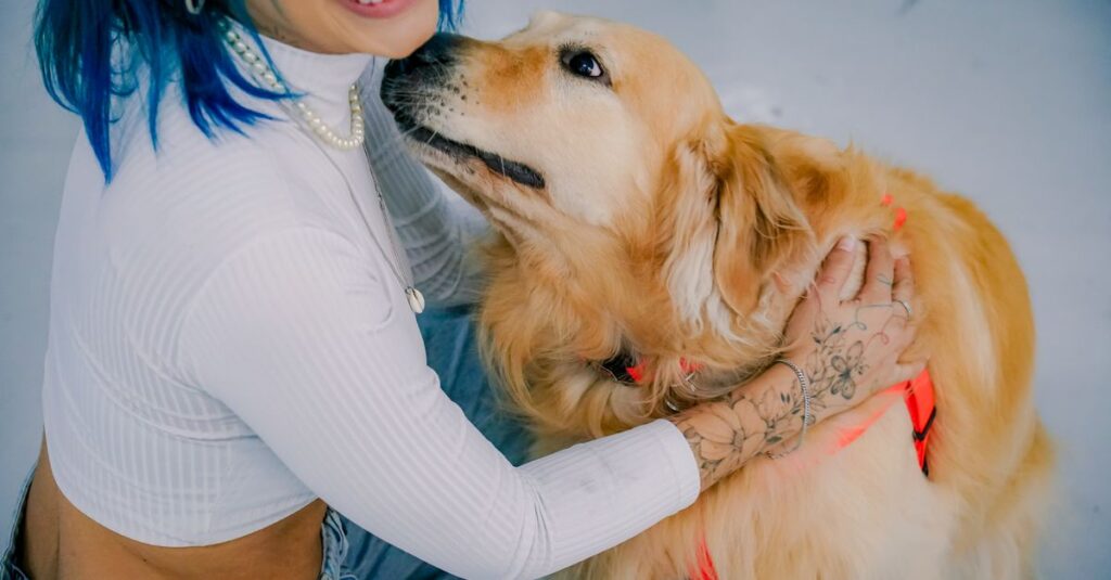 Smiling woman with dyed hair and tattoos embraces her happy golden retriever indoors.