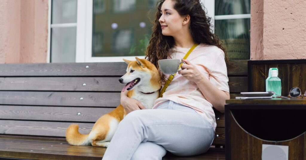 A woman enjoying coffee with her Shiba Inu dog at an outdoor café bench.