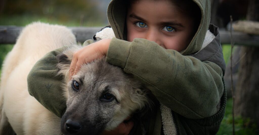 Child in green hoodie lovingly embraces dog, capturing a warm outdoor moment.