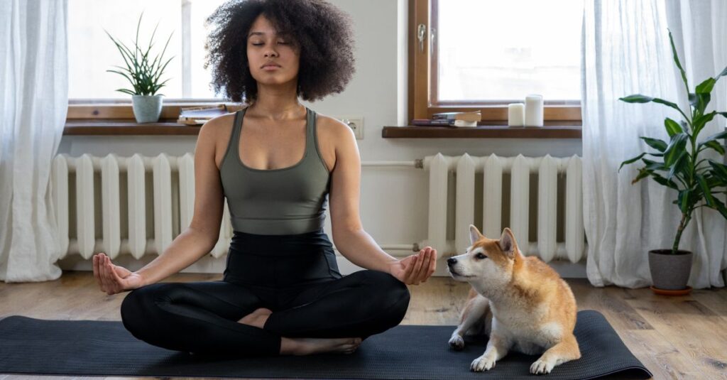 Woman meditating on yoga mat with Shiba Inu dog indoors. Calm and serene home setting.