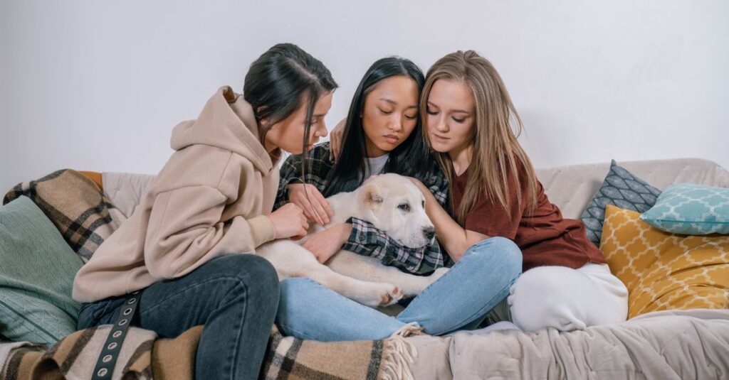 Three women sitting on a couch comforting with a dog, symbolizing support and friendship.