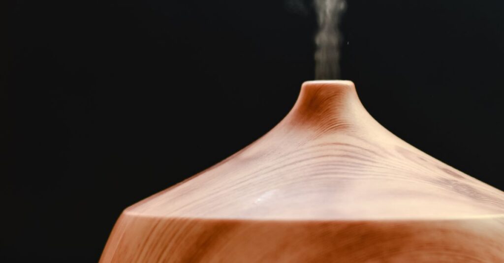 A wooden diffuser releasing calming steam against a black background, ideal for relaxation and aromatherapy stock images.