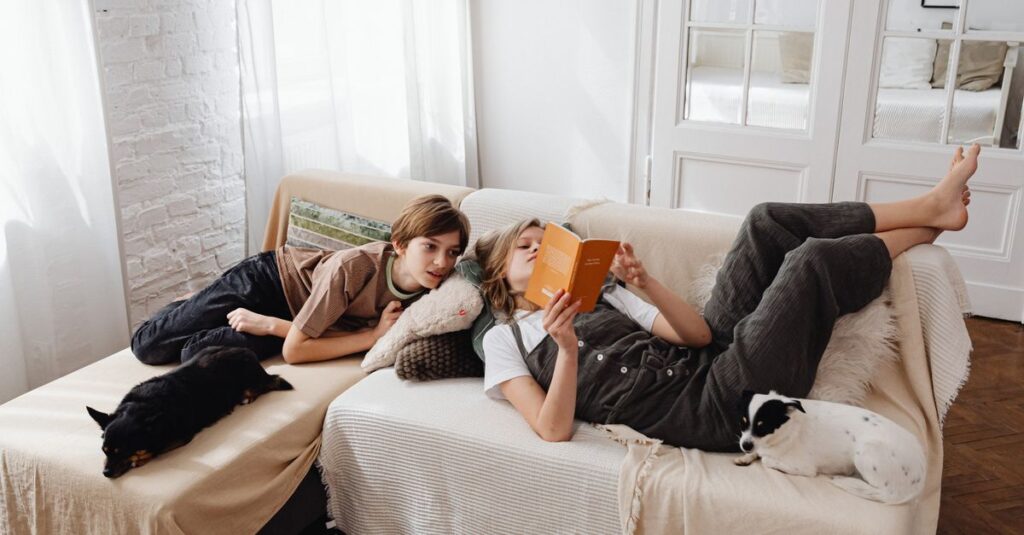 Kids relaxing on the sofa with dogs, enjoying a book in a warm, indoor setting.